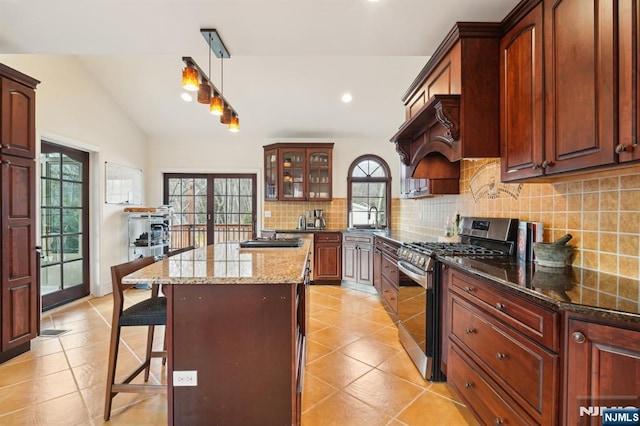 kitchen with lofted ceiling, french doors, stainless steel gas range, a center island, and tasteful backsplash