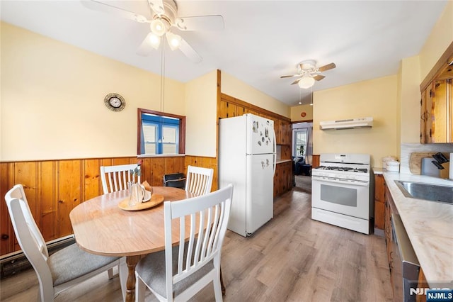 kitchen featuring white appliances, plenty of natural light, wainscoting, under cabinet range hood, and a sink