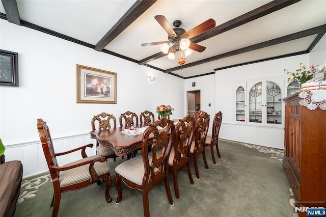 carpeted dining room with ceiling fan, beam ceiling, crown molding, and wainscoting