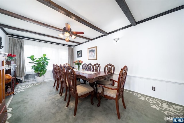 dining space with carpet, beamed ceiling, a wainscoted wall, ornamental molding, and a ceiling fan