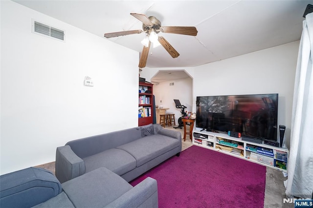 living room featuring carpet flooring, a ceiling fan, visible vents, and arched walkways