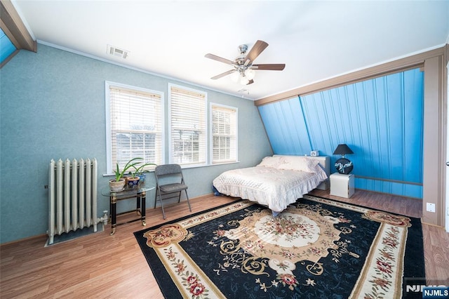 bedroom with visible vents, radiator, ceiling fan, lofted ceiling, and wood finished floors