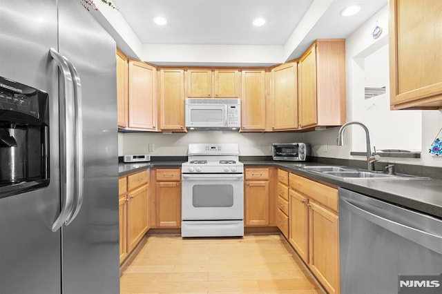 kitchen with a sink, dark countertops, light wood-style floors, and stainless steel appliances