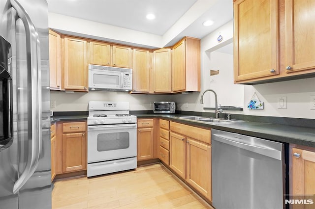 kitchen with recessed lighting, a sink, stainless steel appliances, light wood-style floors, and dark countertops