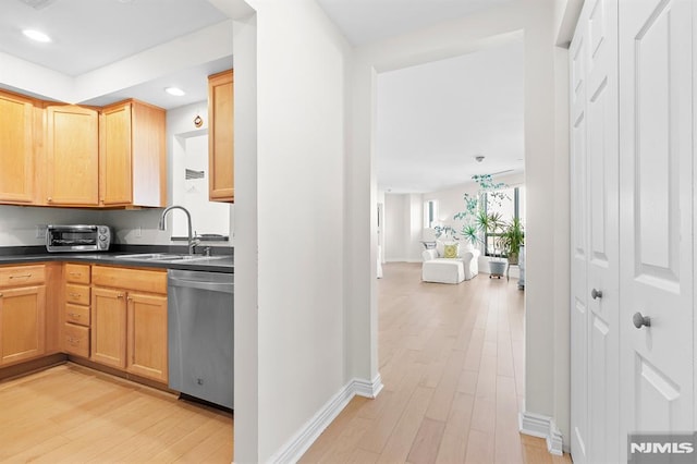 kitchen with a sink, stainless steel dishwasher, dark countertops, and light wood finished floors