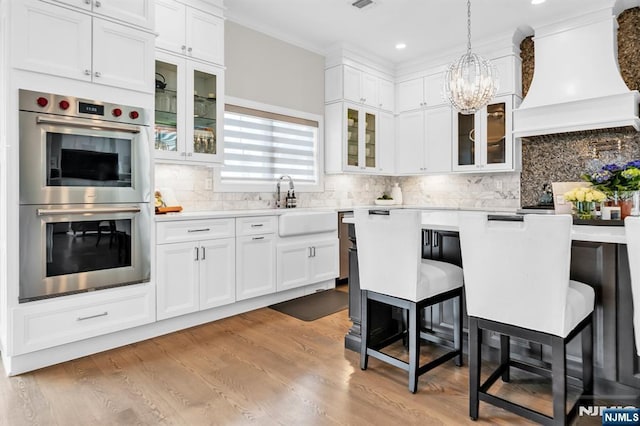 kitchen with light wood finished floors, custom exhaust hood, a breakfast bar area, light countertops, and stainless steel double oven