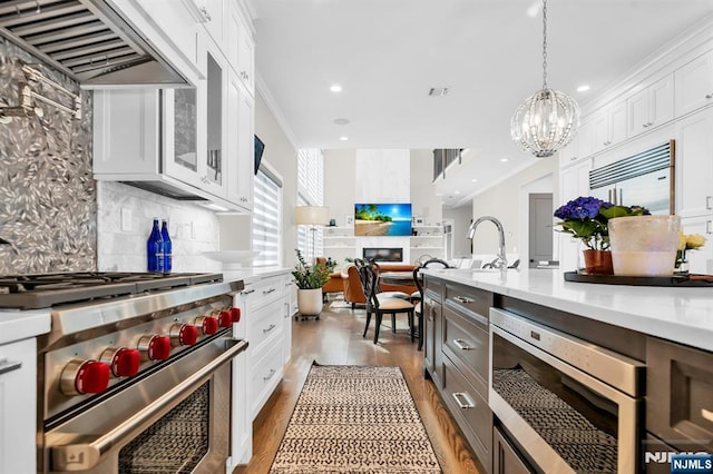 kitchen featuring stainless steel appliances, exhaust hood, white cabinets, light countertops, and decorative backsplash