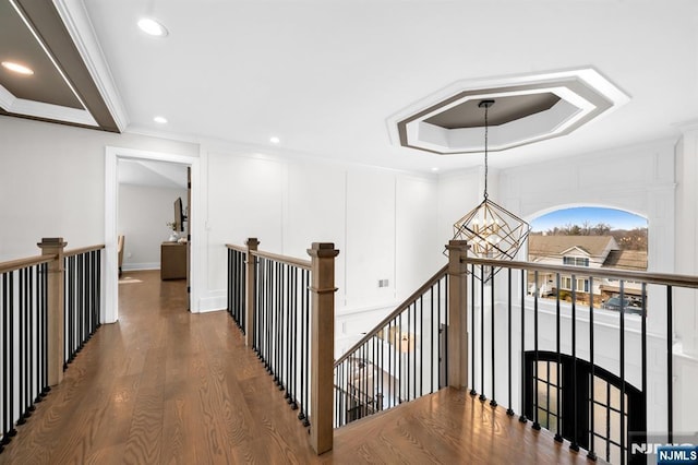 hallway with a tray ceiling, a notable chandelier, ornamental molding, an upstairs landing, and wood finished floors