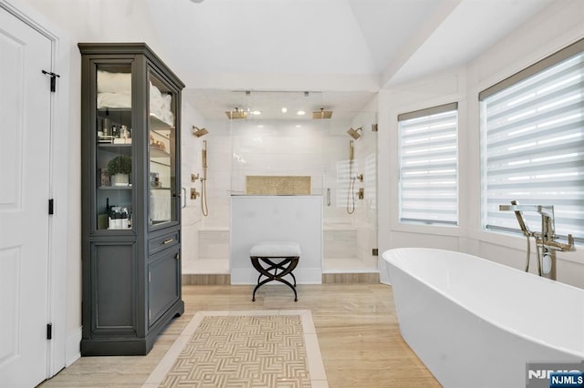 interior space with lofted ceiling, a stall shower, a soaking tub, and wood finished floors