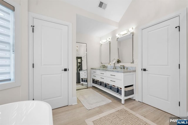 bathroom with wood finished floors, visible vents, vanity, a freestanding bath, and vaulted ceiling