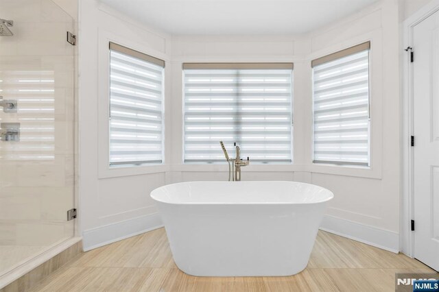 bathroom with a shower stall, a freestanding bath, baseboards, and a wealth of natural light