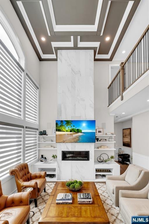 living area with a high ceiling, coffered ceiling, crown molding, and a high end fireplace