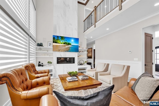 living area featuring built in shelves, recessed lighting, a high ceiling, a premium fireplace, and crown molding