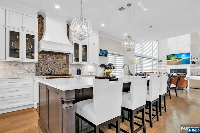 kitchen featuring visible vents, premium range hood, a kitchen island with sink, and tasteful backsplash