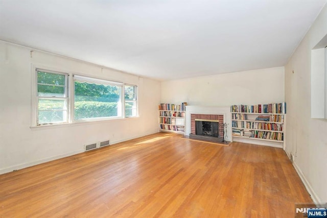 unfurnished living room with baseboards, a fireplace, visible vents, and wood finished floors