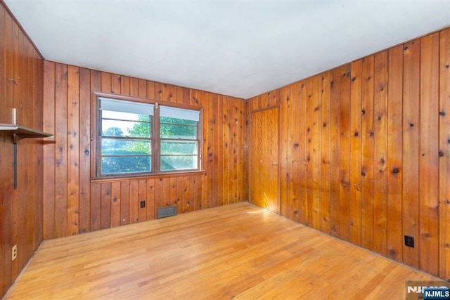 empty room featuring visible vents, wood walls, and wood finished floors