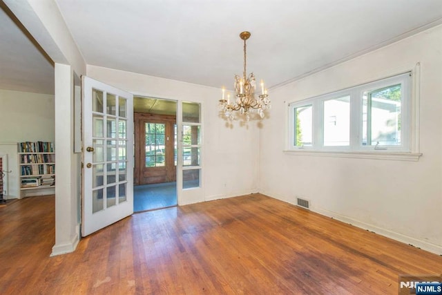 unfurnished dining area with baseboards, french doors, wood finished floors, and an inviting chandelier