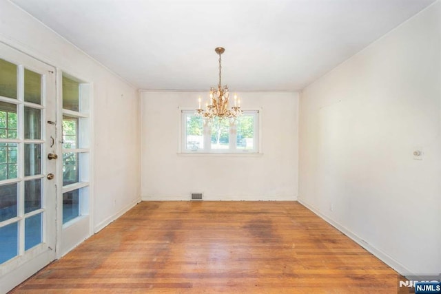 empty room featuring a chandelier, visible vents, baseboards, and wood finished floors