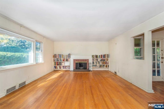 unfurnished living room featuring a brick fireplace, wood finished floors, and visible vents