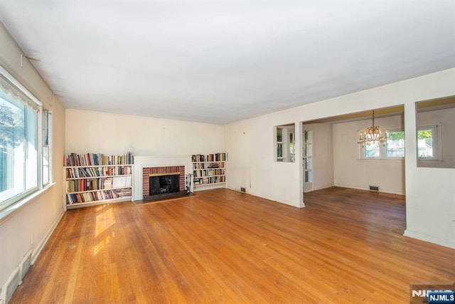 unfurnished living room featuring light wood-style floors, a fireplace, visible vents, and a notable chandelier