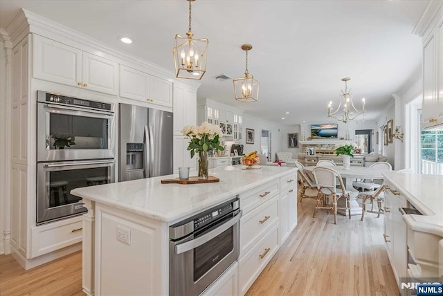 kitchen with a chandelier, stainless steel appliances, ornamental molding, and white cabinetry