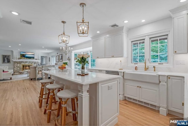 kitchen featuring a stone fireplace, light wood-style flooring, a sink, visible vents, and white cabinets