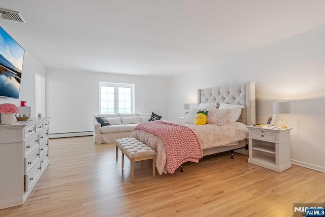 bedroom featuring a baseboard heating unit, light wood-type flooring, and visible vents