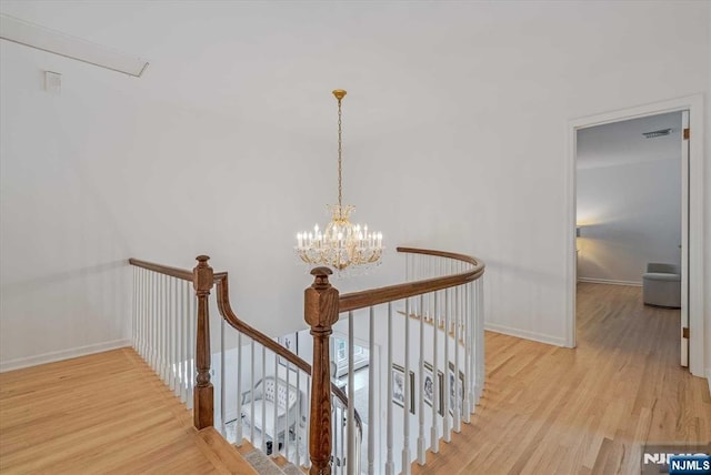 corridor with visible vents, baseboards, wood finished floors, an upstairs landing, and a notable chandelier