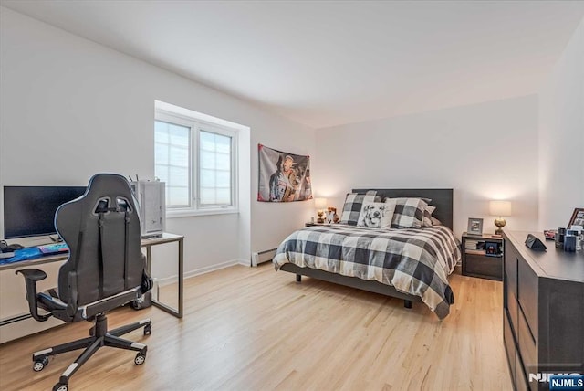 bedroom with baseboard heating, light wood-style flooring, and baseboards