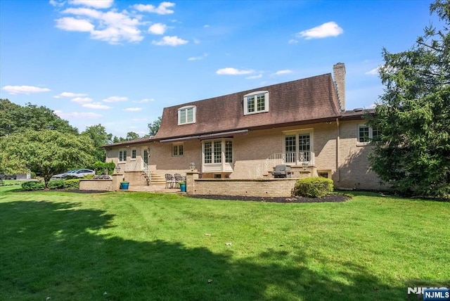 rear view of house featuring a yard, brick siding, a chimney, and a patio