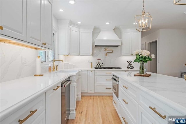 kitchen with appliances with stainless steel finishes, white cabinets, a sink, light wood-type flooring, and premium range hood