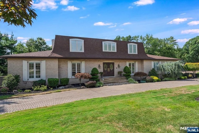 view of front property with brick siding, a front lawn, and a shingled roof