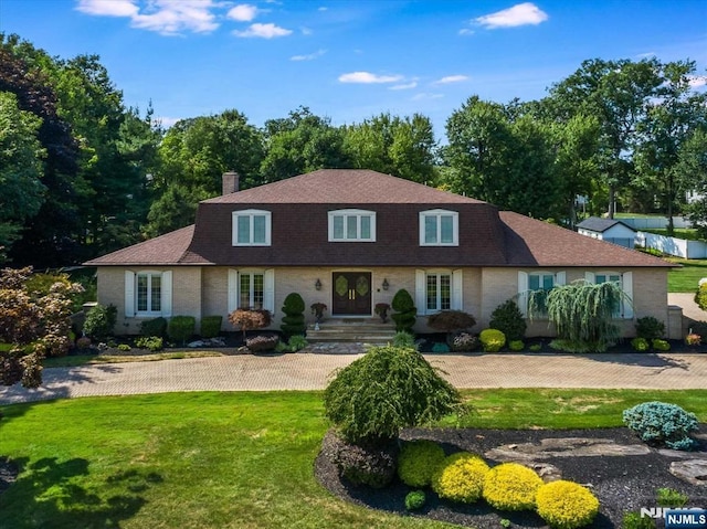 view of front of house with a shingled roof, brick siding, a chimney, and a front lawn