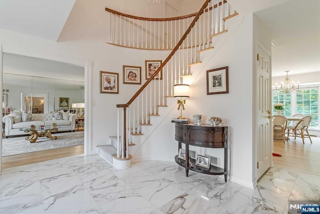 entryway featuring marble finish floor, a notable chandelier, baseboards, and stairs