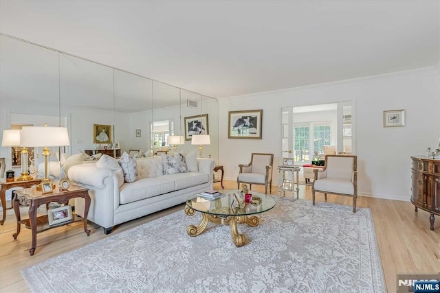 living area with light wood-style flooring, visible vents, baseboards, and ornamental molding