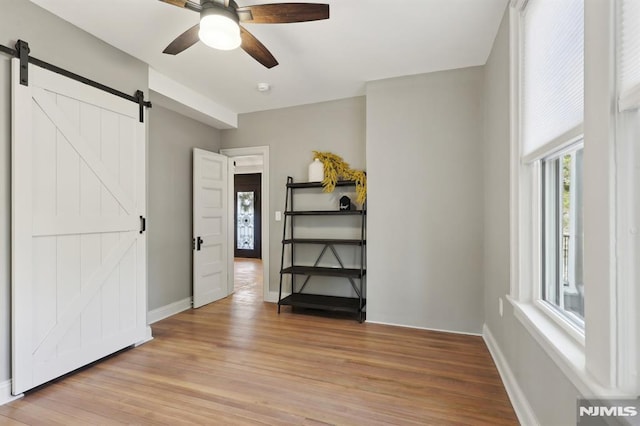 unfurnished bedroom featuring ceiling fan, baseboards, light wood-style floors, and a barn door