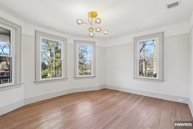 unfurnished room featuring visible vents, baseboards, an inviting chandelier, and hardwood / wood-style floors