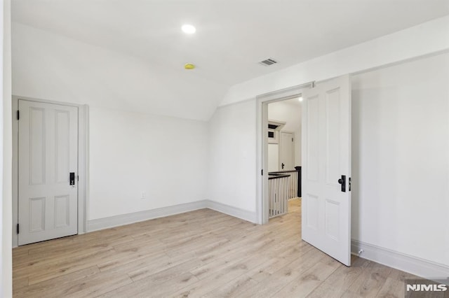 unfurnished room with baseboards, light wood-type flooring, lofted ceiling, and visible vents