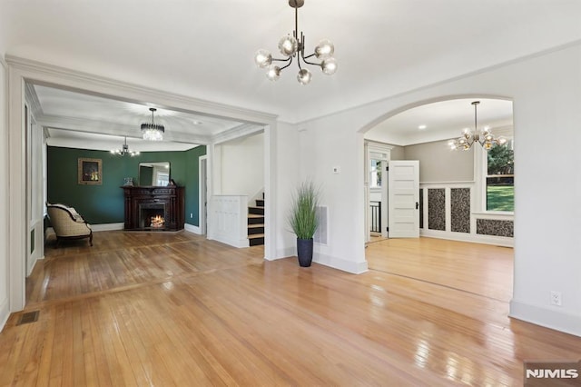 unfurnished living room with stairway, a notable chandelier, wood-type flooring, and a lit fireplace