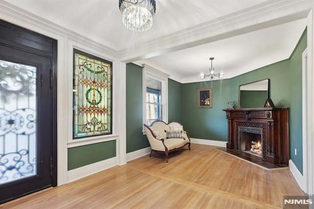 sitting room featuring wood finished floors, baseboards, a lit fireplace, and a chandelier