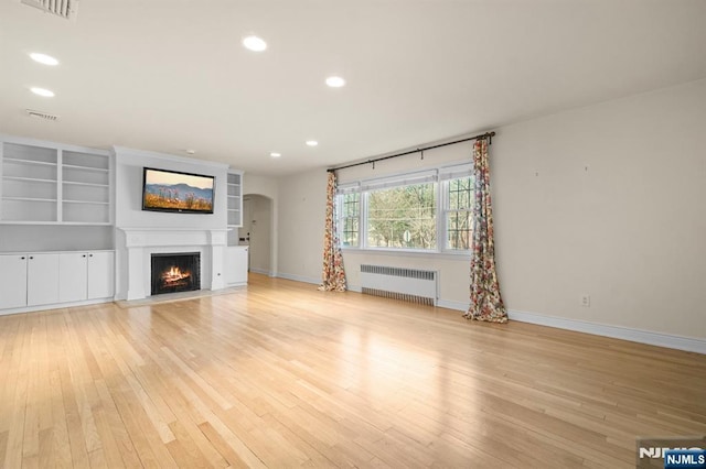 unfurnished living room featuring radiator heating unit, light wood-style floors, visible vents, and a lit fireplace