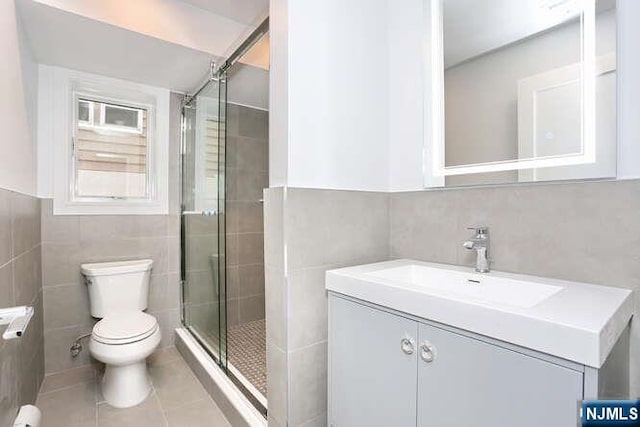 bathroom featuring toilet, tile patterned flooring, vanity, a shower stall, and tile walls