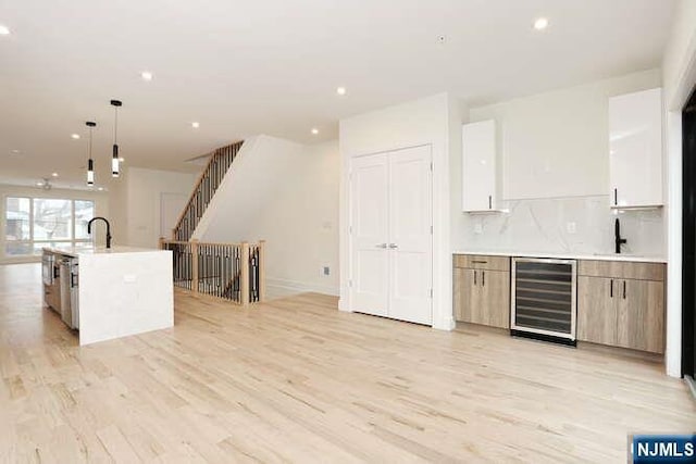 kitchen featuring wine cooler, decorative backsplash, light wood-style floors, a sink, and modern cabinets