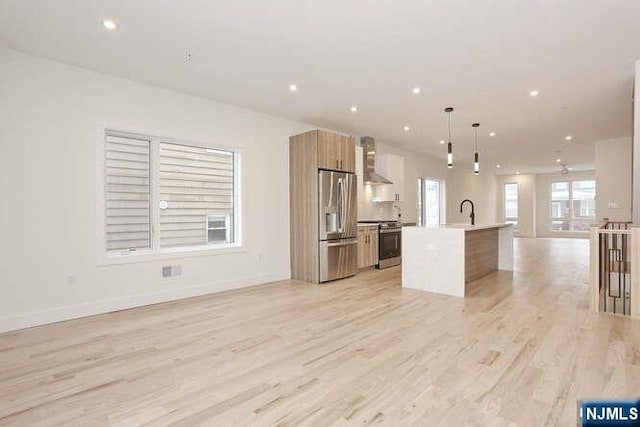 kitchen featuring light wood-style flooring, modern cabinets, open floor plan, stainless steel appliances, and wall chimney range hood