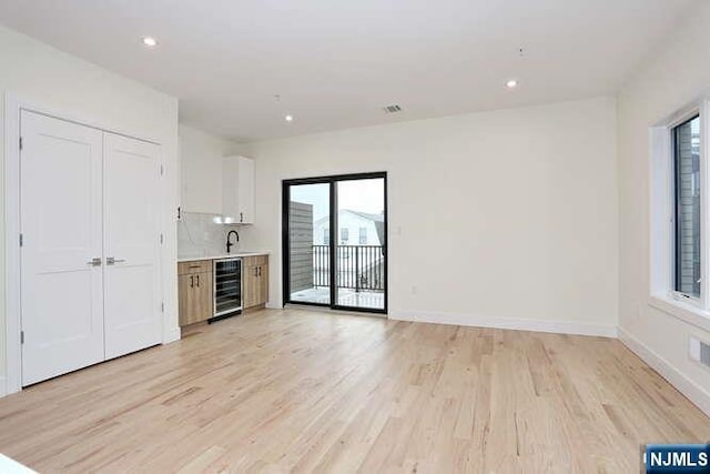 unfurnished living room featuring baseboards, light wood-style flooring, wine cooler, a sink, and recessed lighting