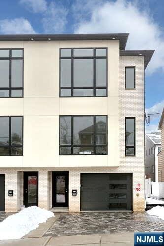 modern home featuring decorative driveway, brick siding, an attached garage, and stucco siding