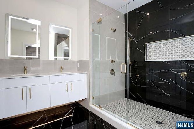 bathroom with double vanity, a shower stall, tile walls, and a sink