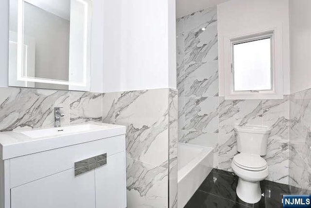 bathroom with a washtub, vanity, toilet, and tile walls