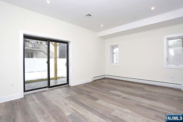 empty room with baseboards, visible vents, baseboard heating, and wood finished floors