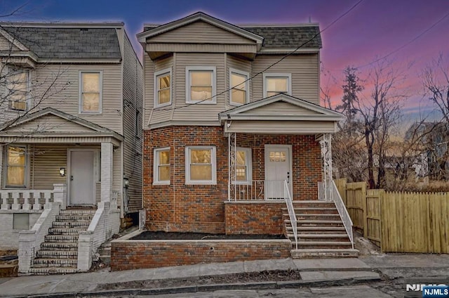 view of front of home with a porch, fence, and brick siding